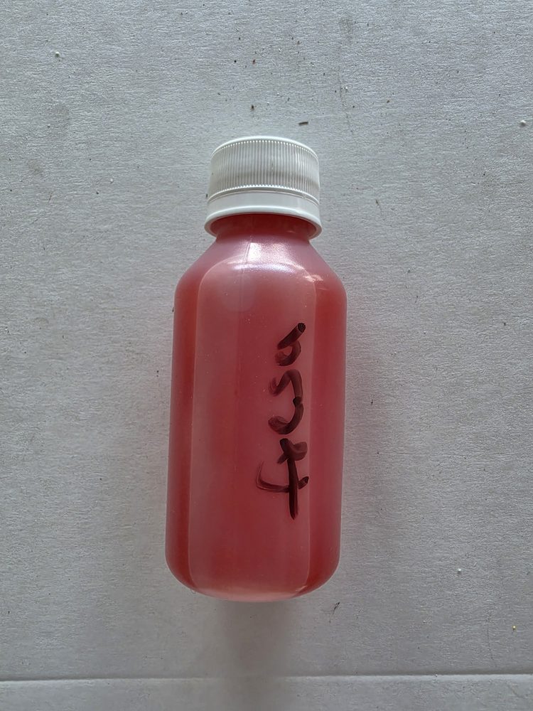 Botella plastica pequeña con esencia liquida color rosado, tapa blanca