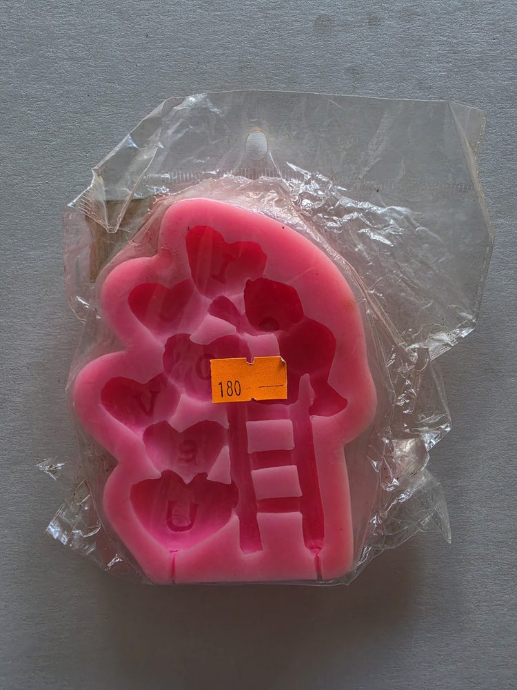 Molde de silicón rosado con varias cavidades de corazones, letras