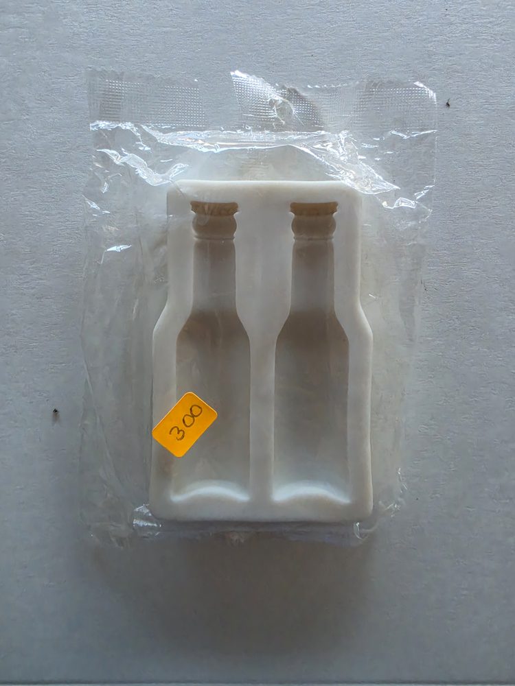 Molde de silicón blanco con dos cavidades en forma de botella, dentro